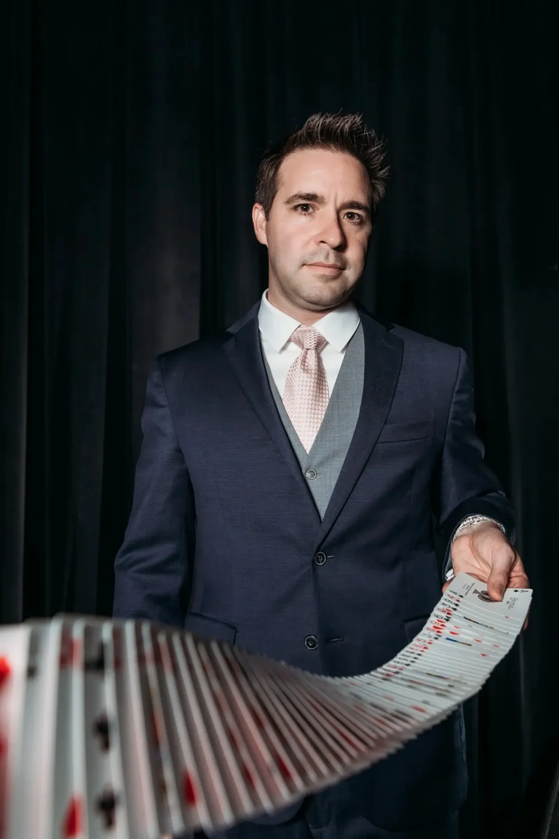 Matt Wilson in a navy suit, spreading a deck of cards in a wide ribbon across the frame