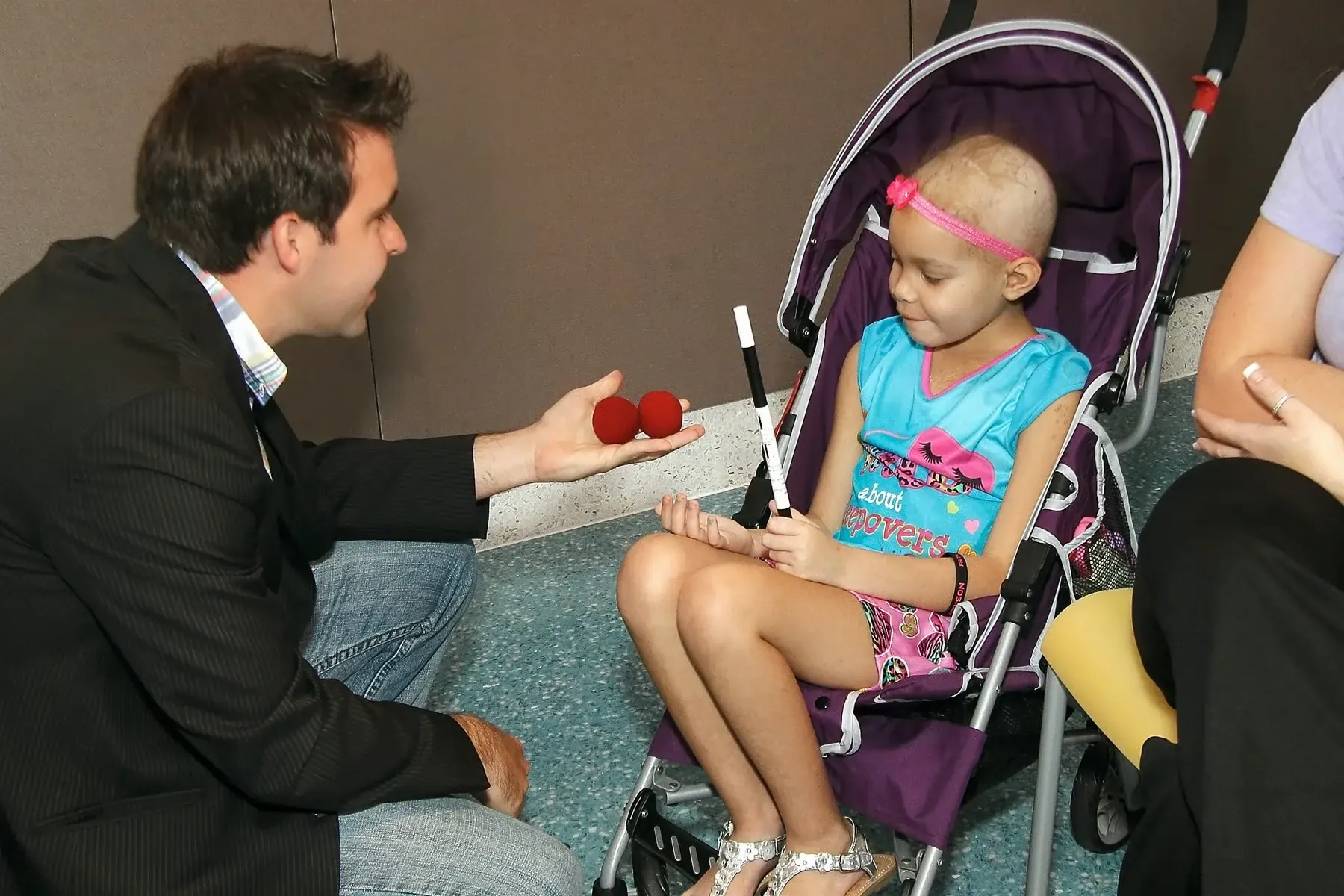 Matt kneeling beside a young hospital patient to show her a trick