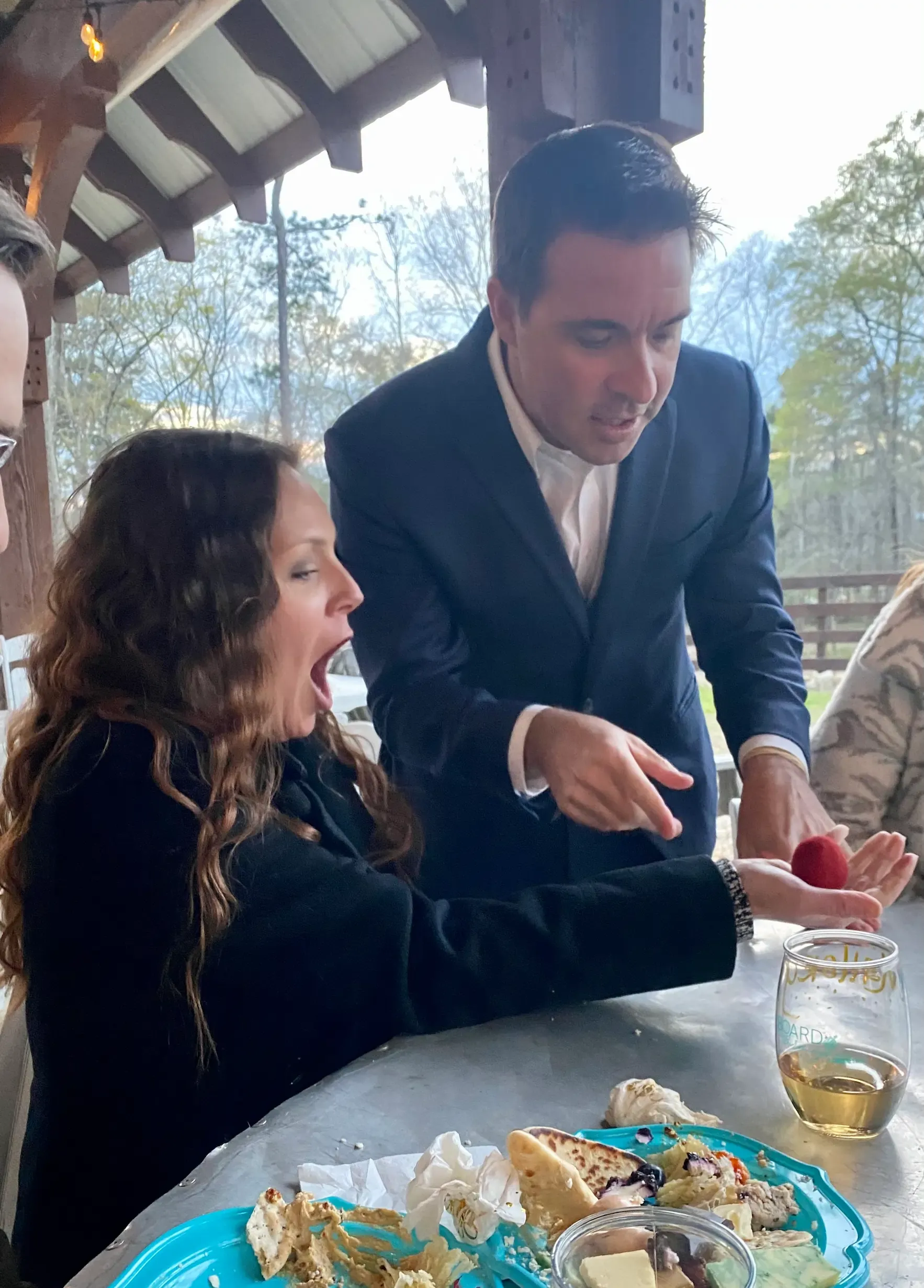 A woman at a dinner table gasping as Matt makes a red ball appear in her hand