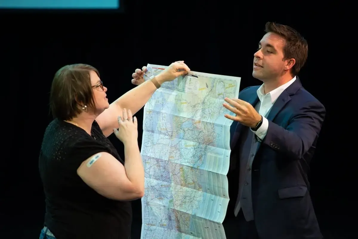 Matt on a dark stage with a volunteer holding an unfolded road map between them