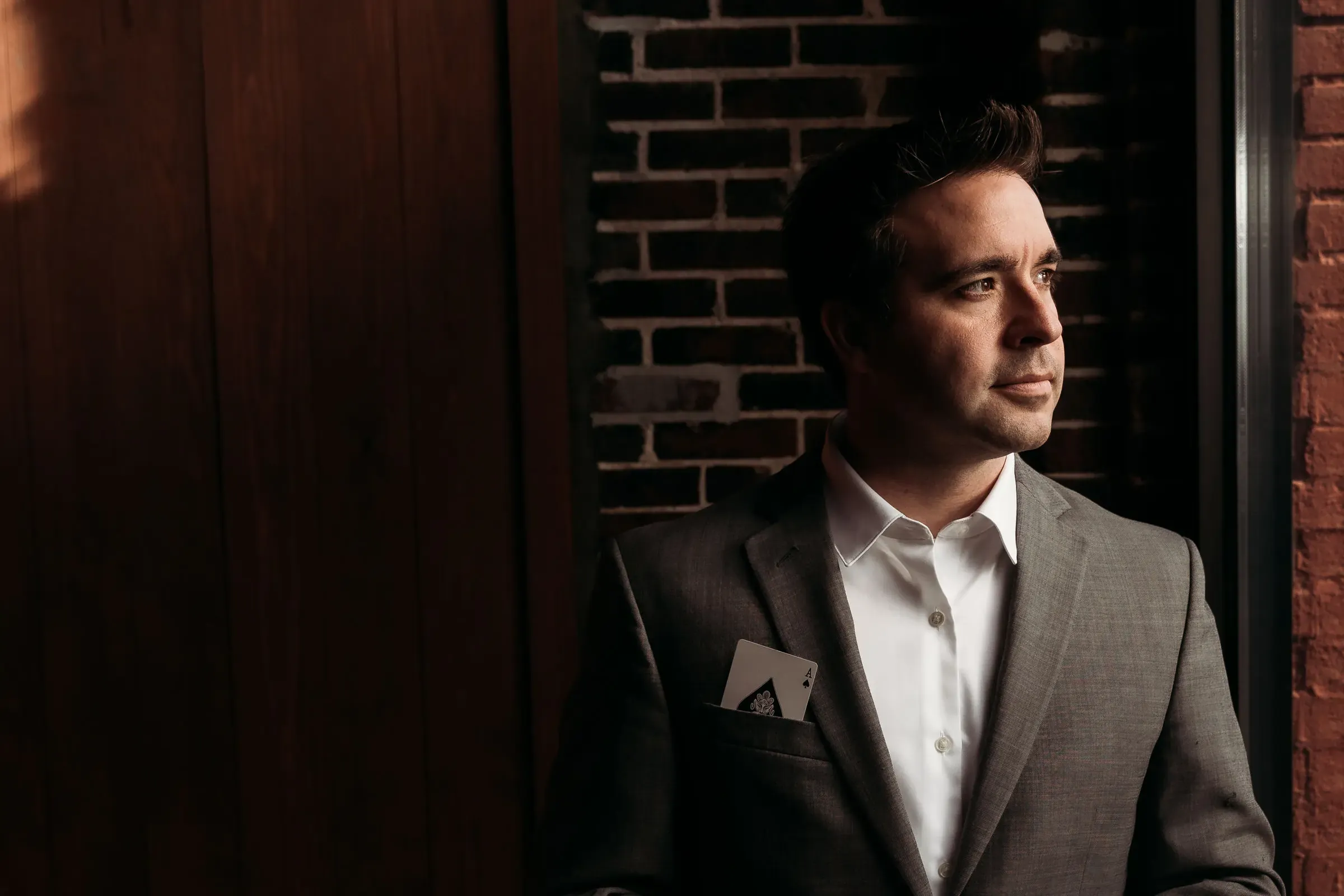 Matt Wilson in a dark suit against a brick wall, looking off-camera.