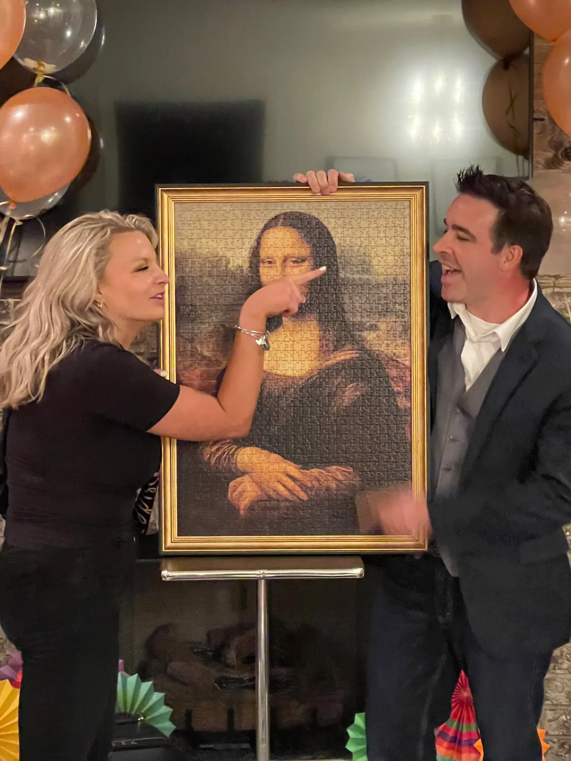 A guest pointing at a framed jigsaw portrait and laughing beside Matt at a parlor show