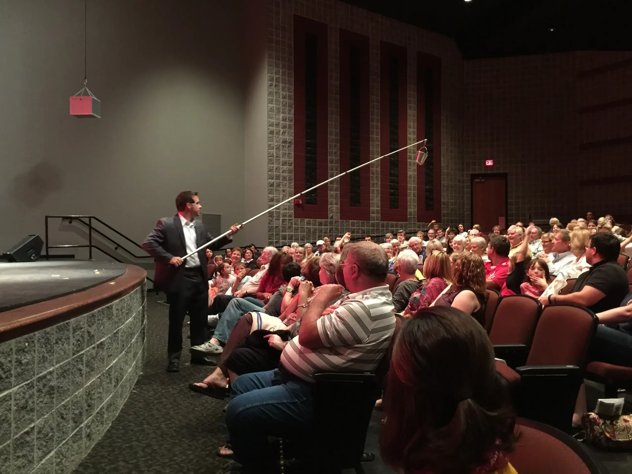 Matt reaching a bucket on a long rod out over a packed theatre audience